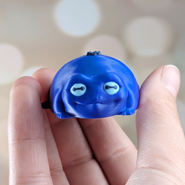 Close-up of Blueberry Frog being held between fingers, front view with detail on eyes and facial features.