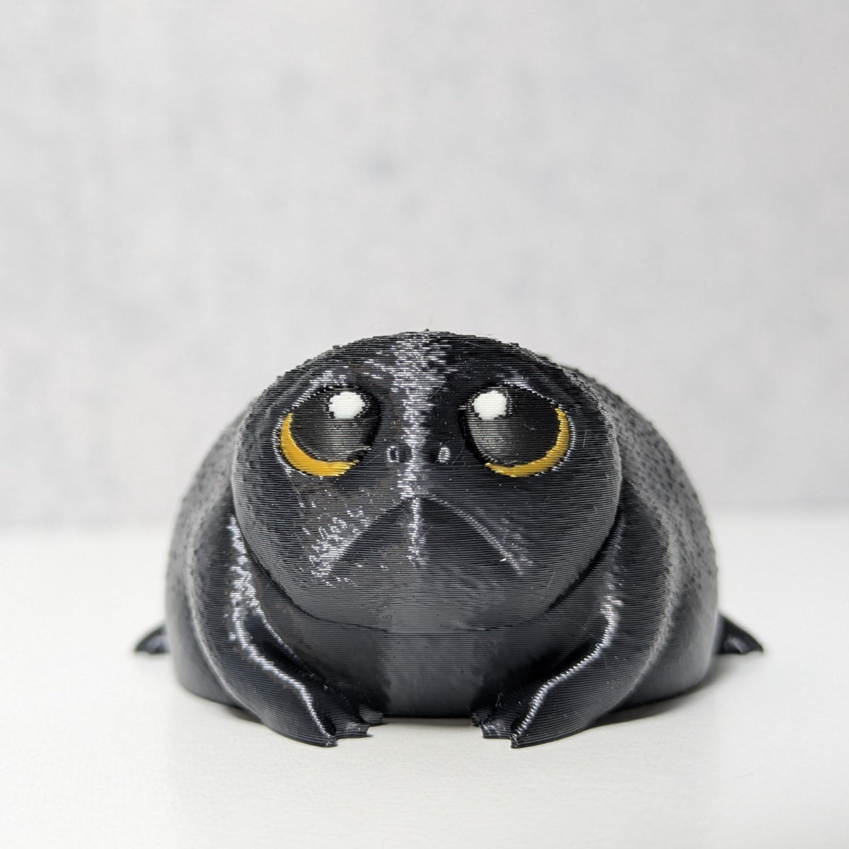 Close-up of a tiny, grumpy black frog figurine, nicknamed Depressed Dumpling, with a hopeless stare.