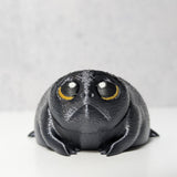 Close-up of a tiny, grumpy black frog figurine, nicknamed Depressed Dumpling, with a hopeless stare.