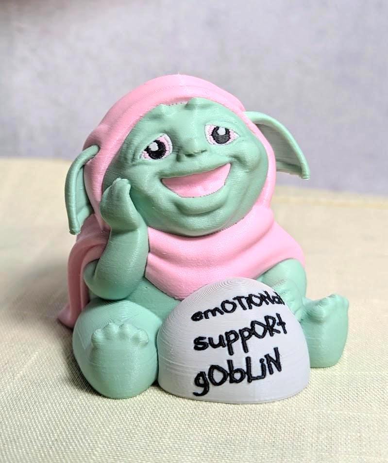 Front-facing view of Emotional Support Goblin™ smiling with a small rock that says Emotional Support Goblin.