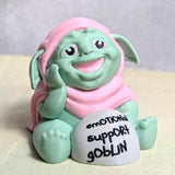 Front-facing view of Emotional Support Goblin™ smiling with a small rock that says Emotional Support Goblin.