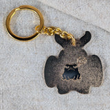 Back of Mothman enamel keychain with engraved frog detail on beige background