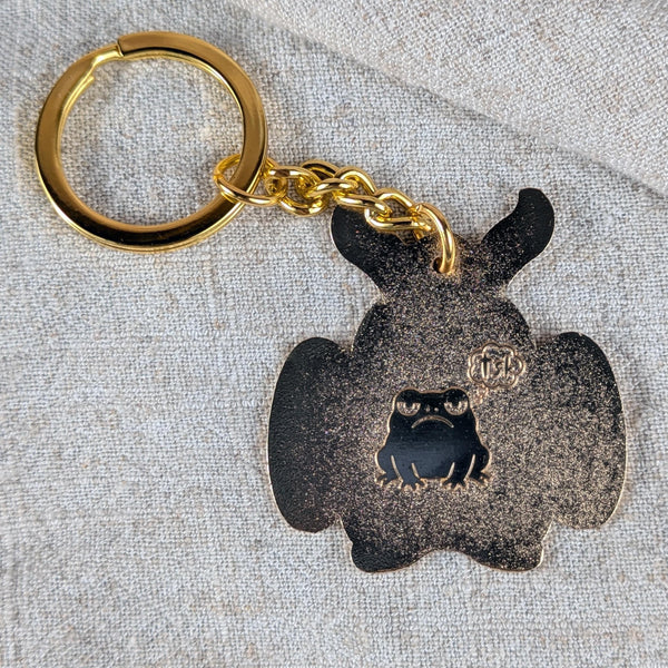 Back of Mothman enamel keychain with engraved frog detail on beige background