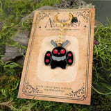 Mothman enamel keychain on branded backing card with mossy background