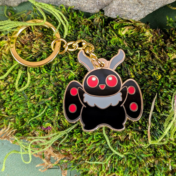 Mothman keychain on moss and rocks for whimsical forest-themed aesthetic