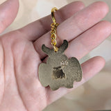 Reverse side of Mothman keychain held in hand showing engraved frog and gold finish