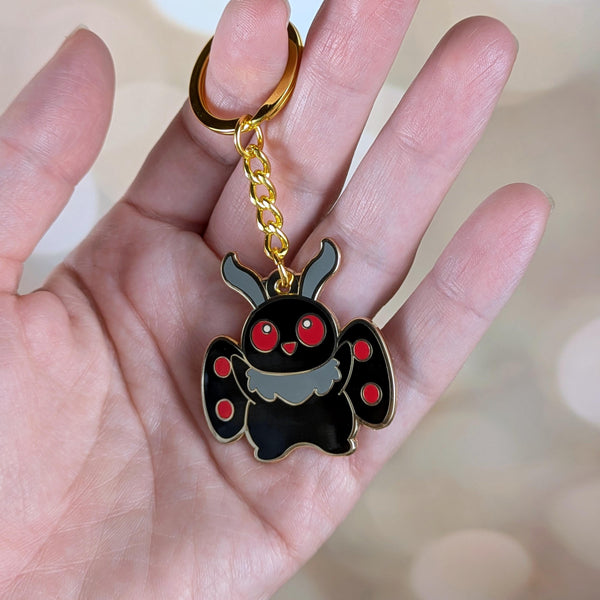 Mothman hard enamel keychain shown in hand for size reference