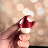 Close-up of the red and white spotted mushroom game piece held in fingers, with smooth glossy finish and rounded cap.