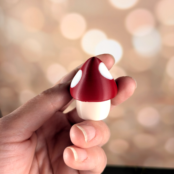 Close-up of the red and white spotted mushroom game piece held in fingers, with smooth glossy finish and rounded cap.