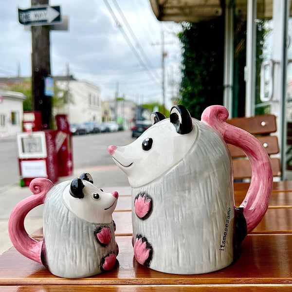 Two possum shaped coffee mugs sitting on a wooden surface.