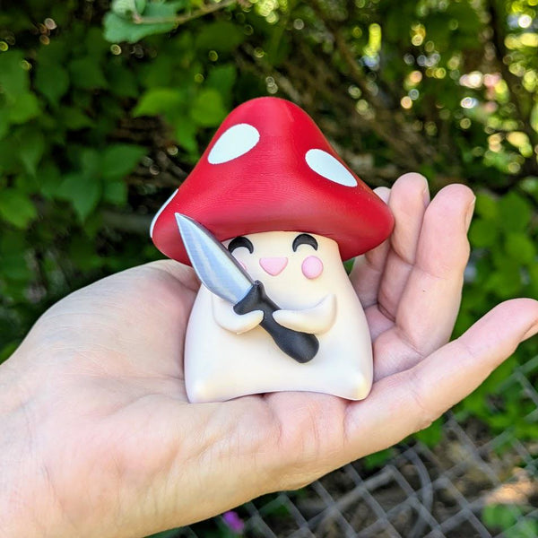 Shroomshank™ held in hand with knife, showing scale and chaotic energy.