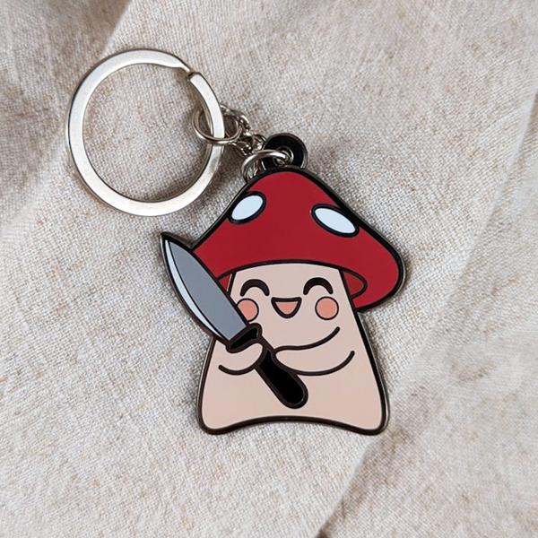 Keychain with cartoon mushroom character holding a knife on a beige fabric background
