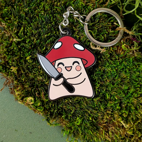Keychain with mushroom character holding a knife on a green moss background