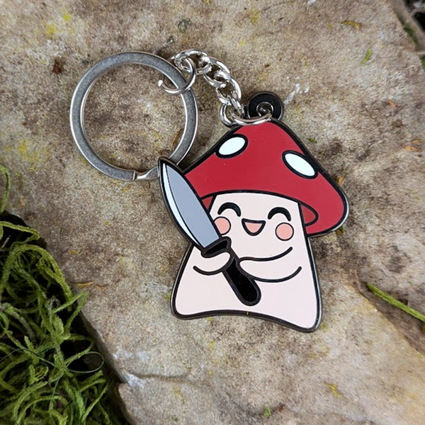 Mushroom shaped enamel bag charm on a stone surface.