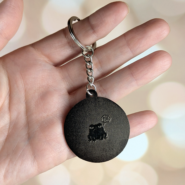 Back of enamel keychain in hand showing engraved frog on silver backing