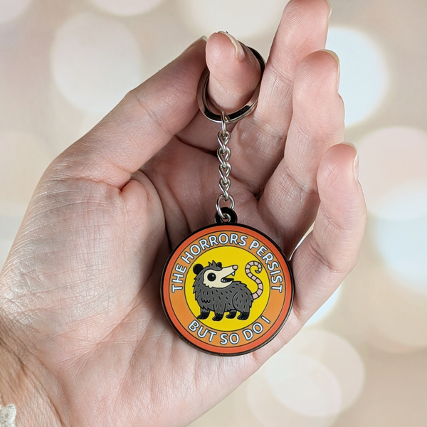 Front of possum keychain in hand showing design and scale