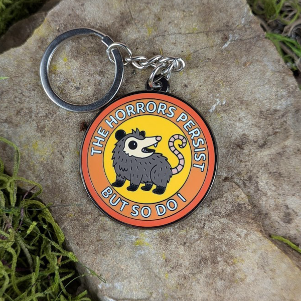Funny enamel possum keychain on stone and moss background